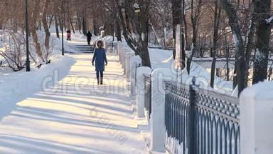 穿着蓝色<strong>羽绒服</strong>的年轻女子，带着毛皮罩在冬季公园散步。 前景。